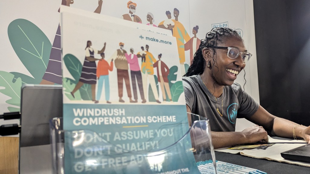 Woman Smiling with flyers for Windrush Compensation scheme